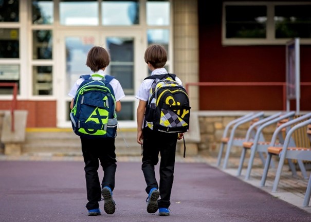 two children with backpacks walking towards a school entrance