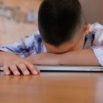 child with head down on a desk, looking tired