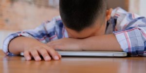 child with head down on a desk, looking tired