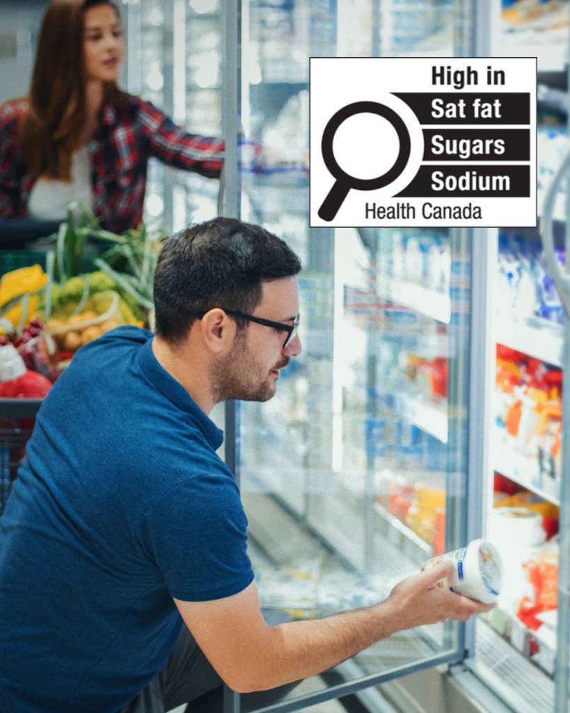 Person looking at container of dairy product, in front of a grocery store cooler