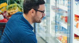 Person looking at container of dairy product, in front of a grocery store cooler